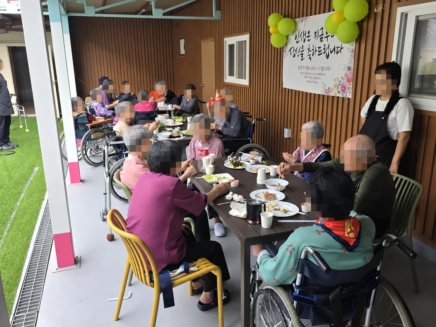 축하 현수막과 풍선 아래에서 함께 식사하는 어르신들