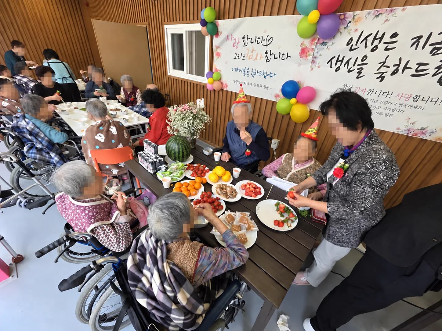 과일과 음식이 차려진 식탁에서 고깔모자를 쓰고 축하를 함께하는 모습