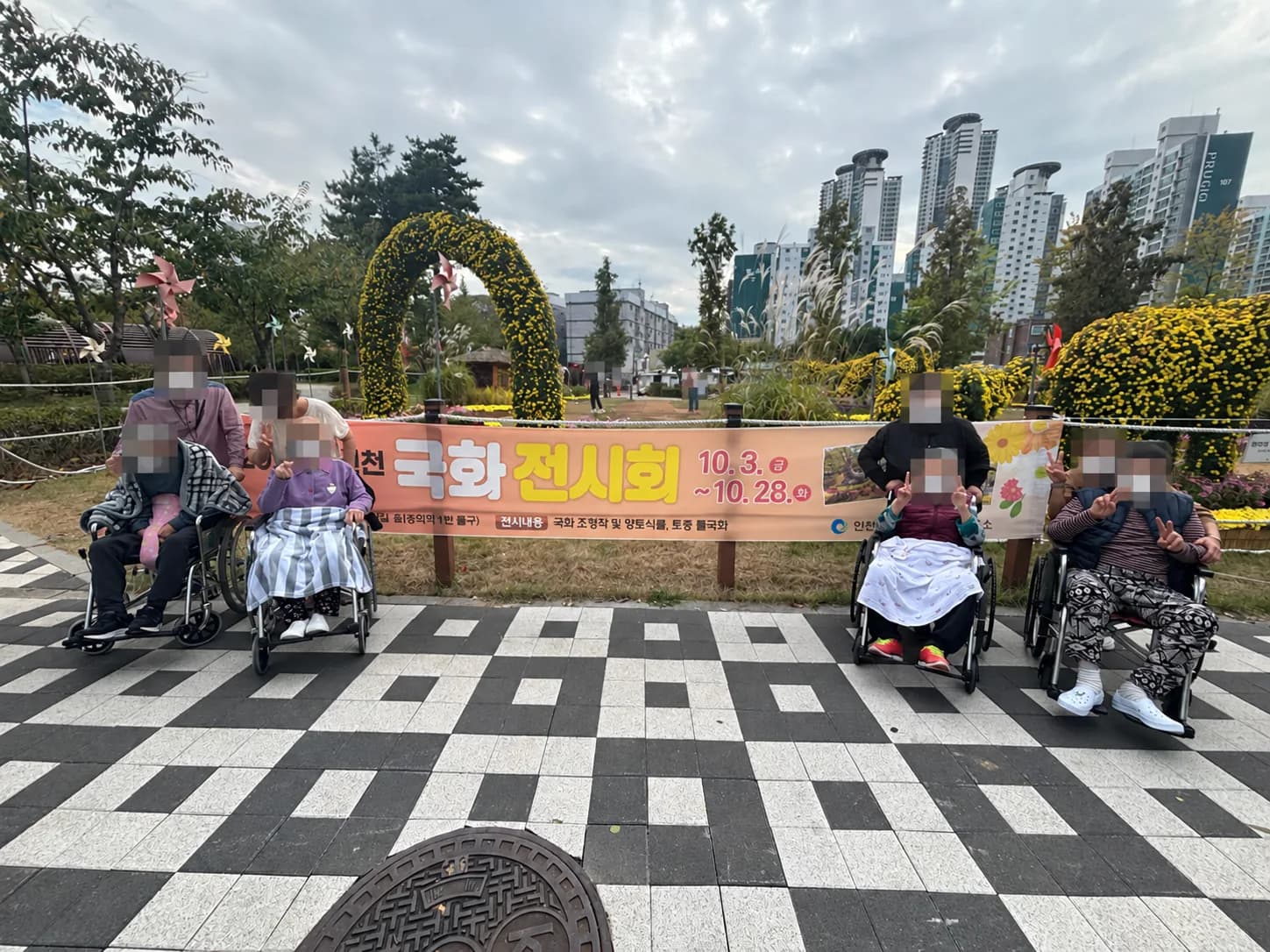 꽃으로 꾸며진 공원 입구에서 나란히 선 어르신과 동행인들